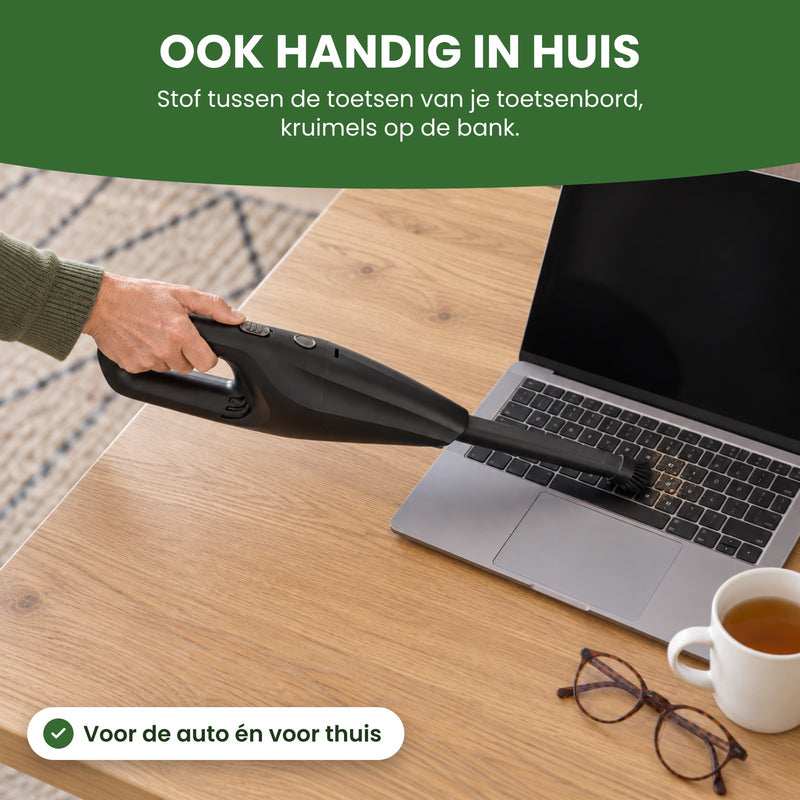 A hand holds the Neatix with its long nozzle and brush over a laptop keyboard on a dining table: handy at home, too